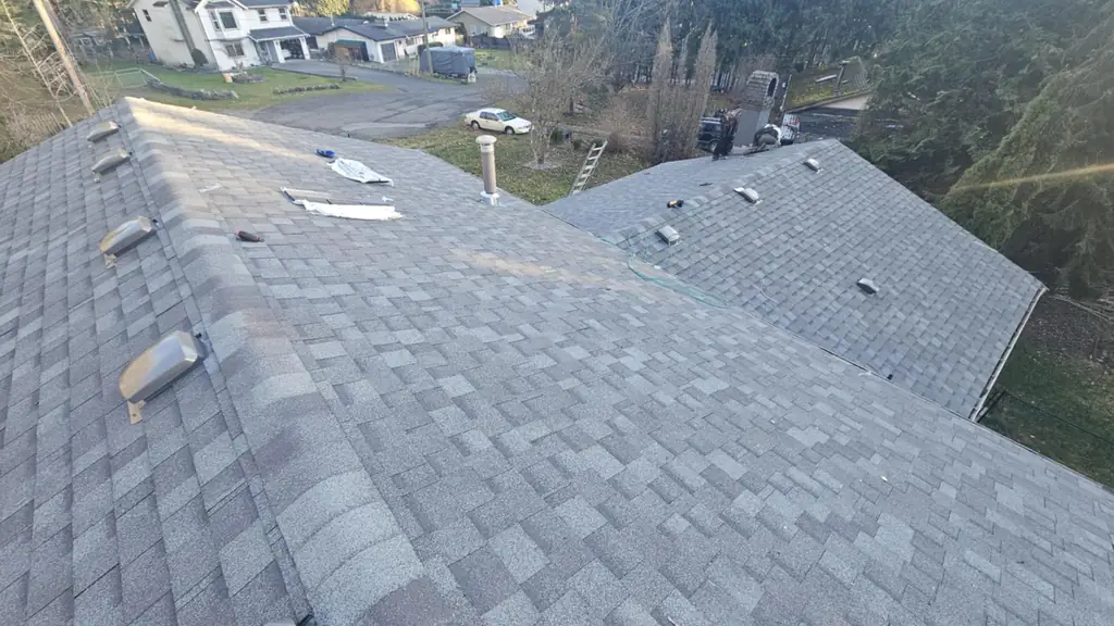 Standing on a gray dimensional shingle roof where two planes meet at a valley, with underlayment scraps and a tool lying on the shingles. Fraser Roofing