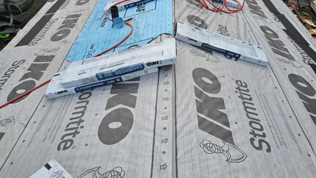 A worker stands at the far end of a roof mostly covered in IKO Stormtite underlayment with a section of blue GAF Deck-Armor underlayment nearby. Fraser Roofing