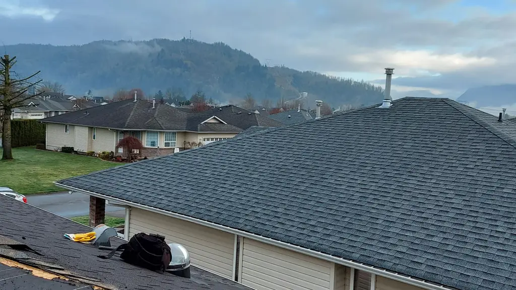 Finished grey hip roof shingled and clean, with a red-handled shingle rake leaning against a pile of old tear-off debris in the foreground. Fraser Roofing