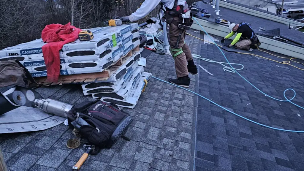 Two roofers work on a large asphalt shingle roof at dusk. Fraser Roofing