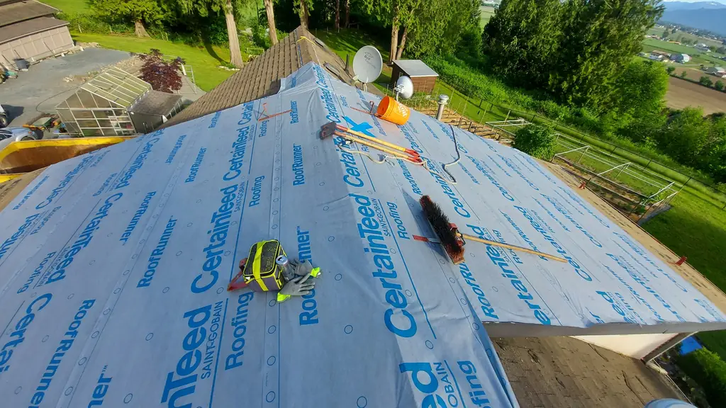Wide view of a roof plane fully covered in blue-and-white printed CertainTeed RoofRunner synthetic underlayment, with a push broom, roofing hatchets. Fraser Roofing