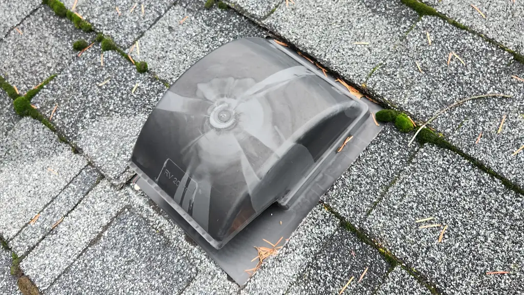 A close, top-down view of a plastic roof vent marked with a partial 'RV 20' label, installed on a grey shingle roof. Fraser Roofing