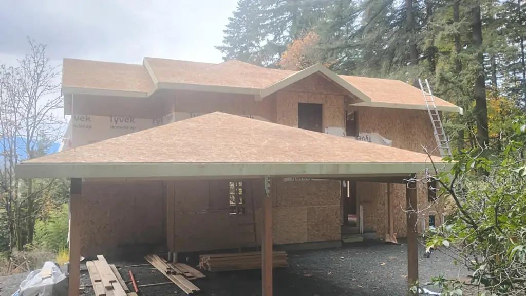 A new two-story house under construction shows its roof sheathed only in bare OSB plywood, not yet shingled. Fraser Roofing