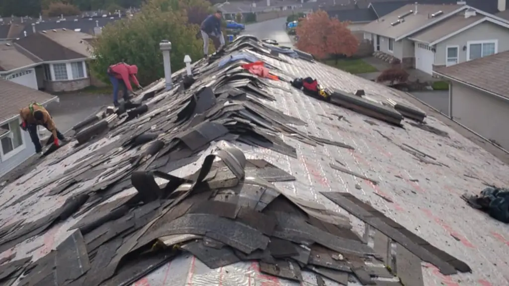 A wide on-roof shot mid tear-off, with large piles of torn-up shingles and felt lying on top of red synthetic underlayment. Fraser Roofing