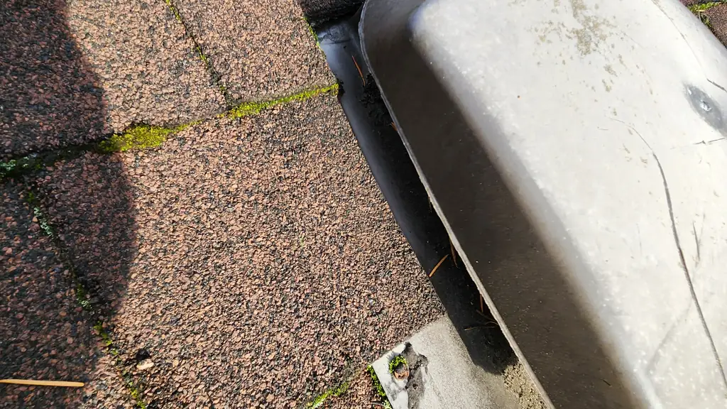 Close-up of a large aluminum roof vent stamped with the word 'VENT' mounted at a roof edge, with moss growing along the nearby hip and ridge lines. Fraser Roofing