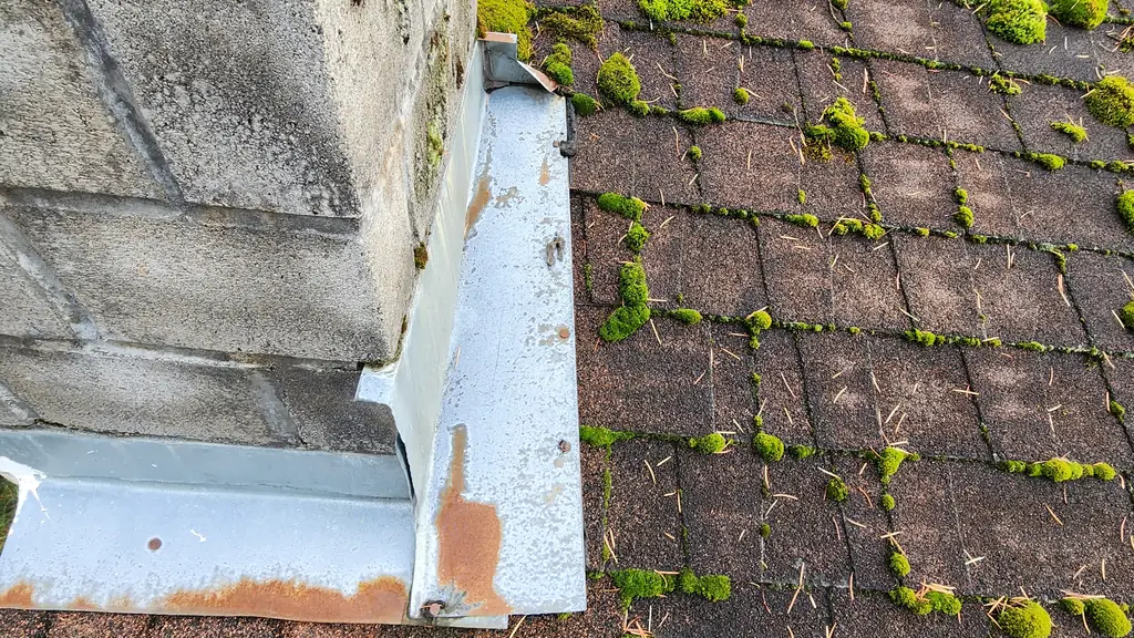 A close view of a concrete-block chimney base with new galvanized step flashing showing some rust staining. Fraser Roofing