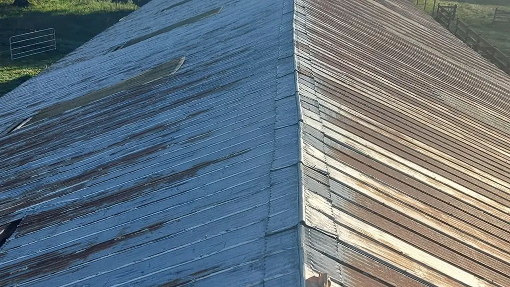 A metal roof ridge runs toward distant mountains, with half the roof surface an aged grey and the other half a rusty brown. Fraser Roofing