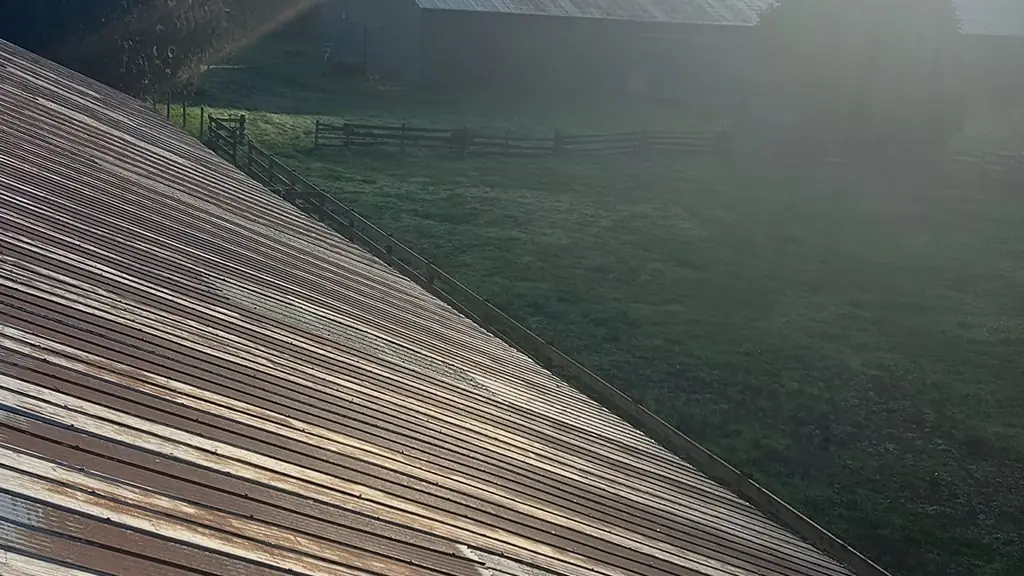 A weathered, rusty corrugated metal roof fills the foreground, catching strong morning sun flare. Fraser Roofing