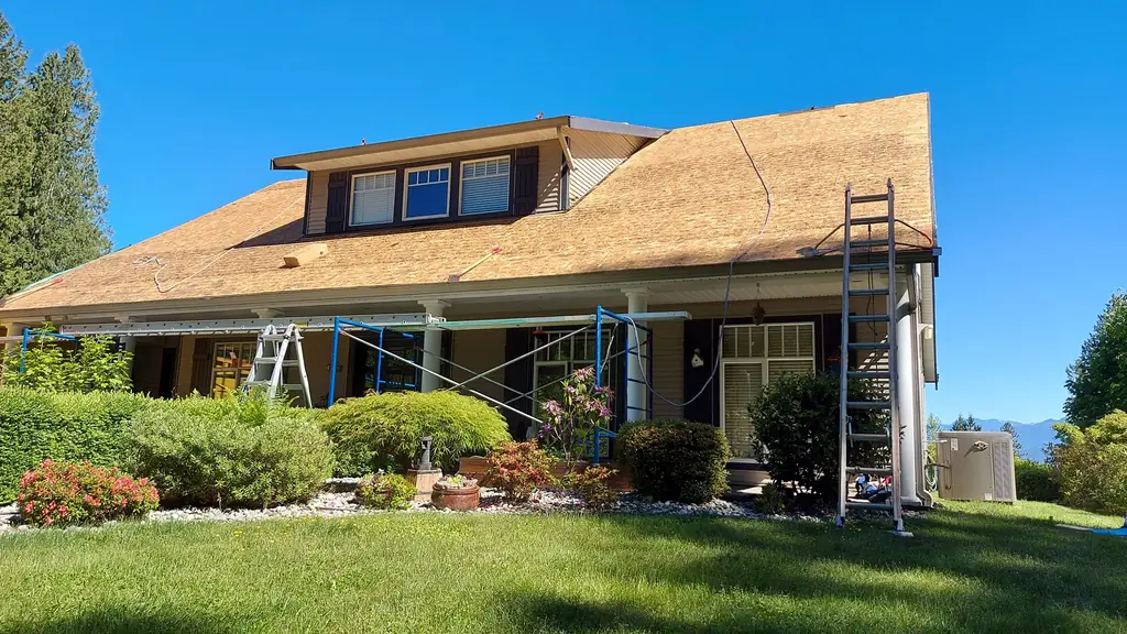 A large two-story house with dark shutters and a wraparound porch is shown from the front lawn. Fraser Roofing