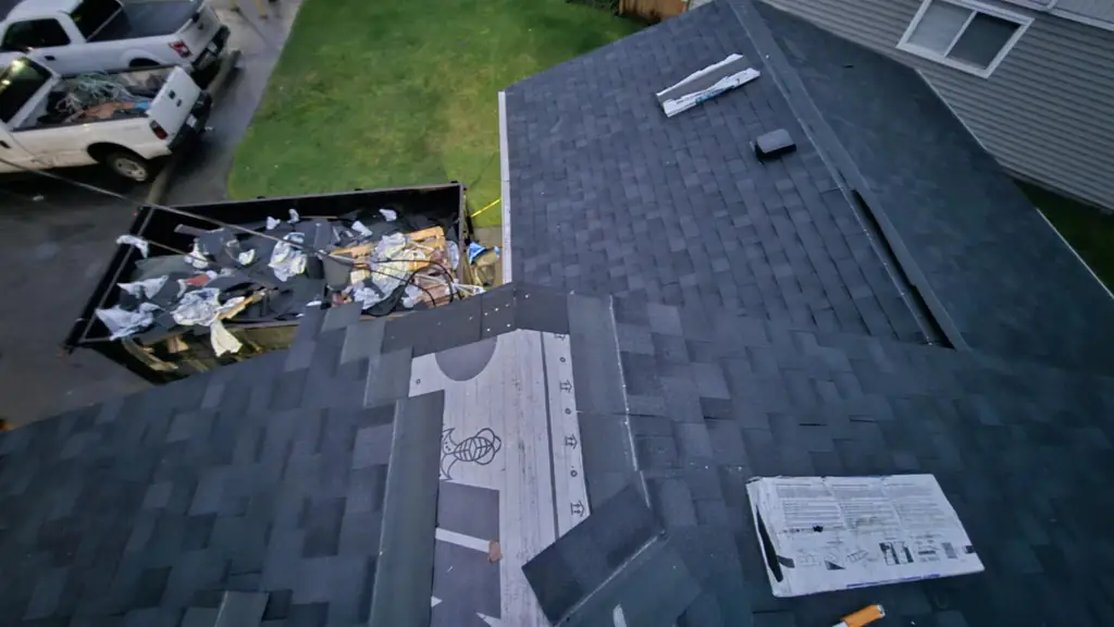 A view down a roof valley toward a dumpster in the driveway below, full of torn-off shingle debris. Fraser Roofing