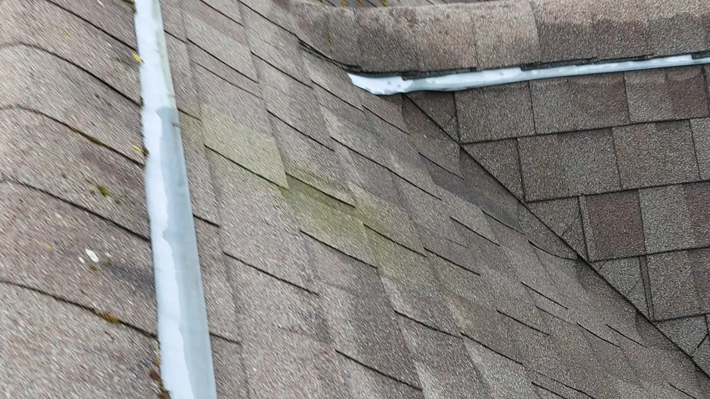 An aged brown asphalt shingle roof valley shows moss streaking down the slope. Fraser Roofing
