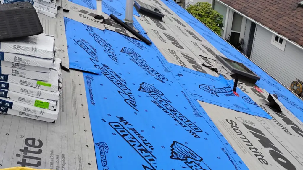 An on-roof shot with bundles of IKO Cambridge shingles staged near the top of frame and a large section of blue Roofnado StormTread and grey IKO. Fraser Roofing