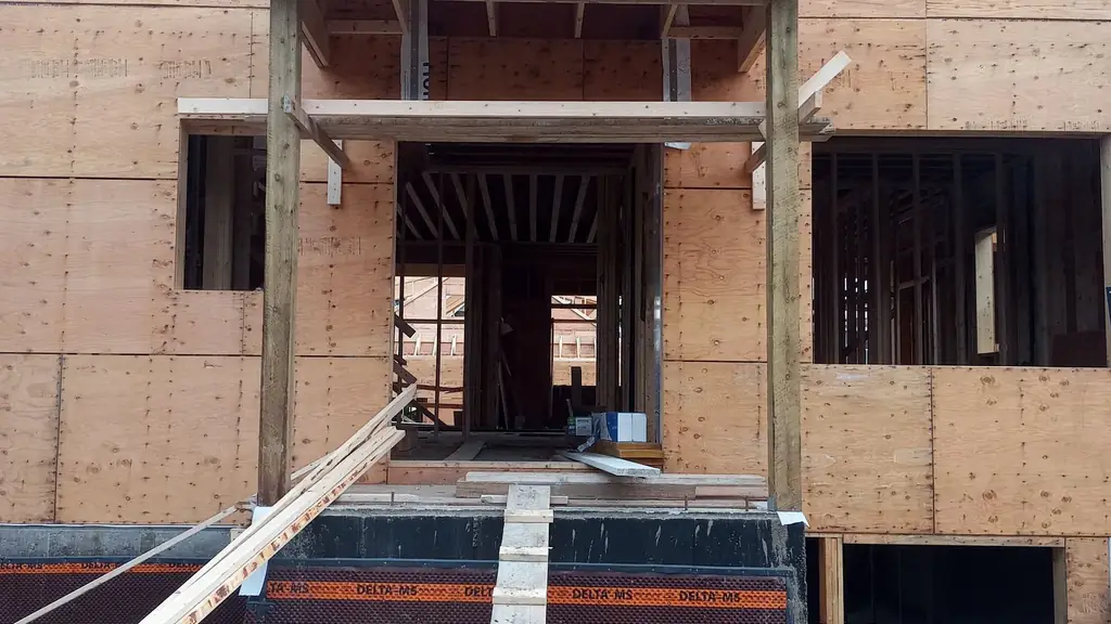 Ground-level view of a two-storey house under construction, plywood-sheathed exterior walls with window and door openings cut. Fraser Roofing