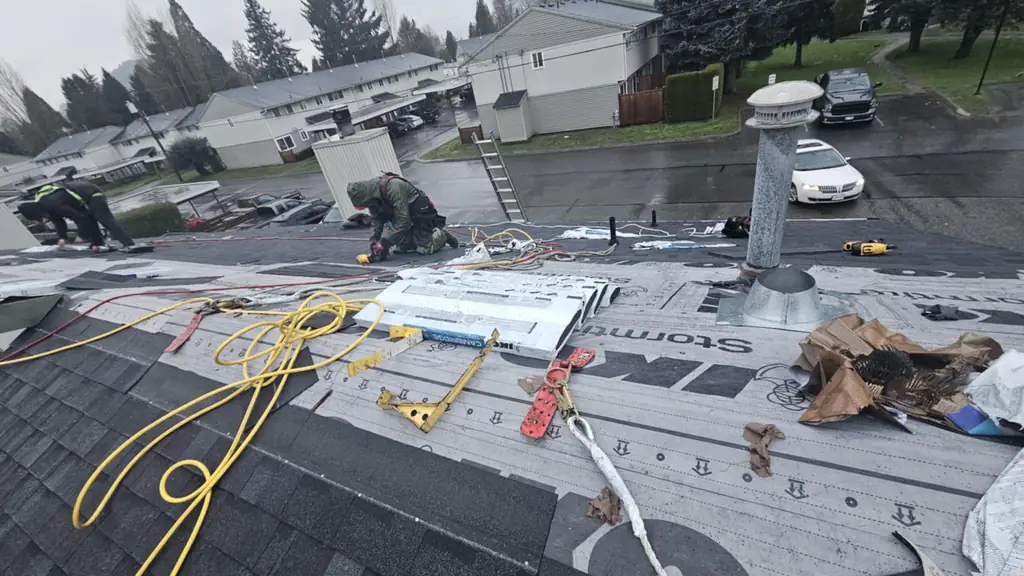 A wide on-roof shot mid-installation with two workers on the ridge, one wearing camo coveralls. Fraser Roofing