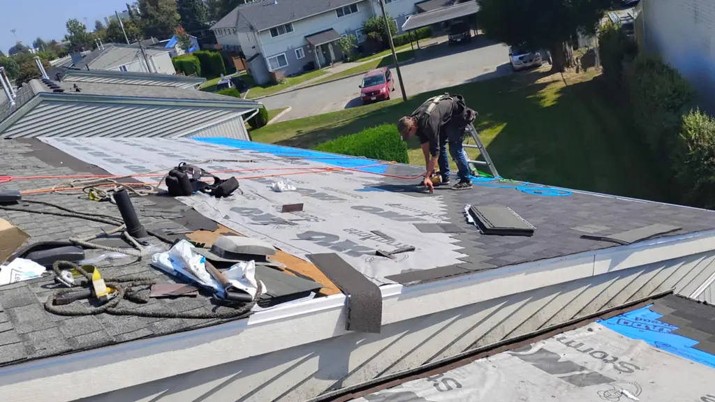 A worker bends over installing grey IKO Stormtite branded underlayment at a roof edge, wearing a tool belt and harness. Fraser Roofing
