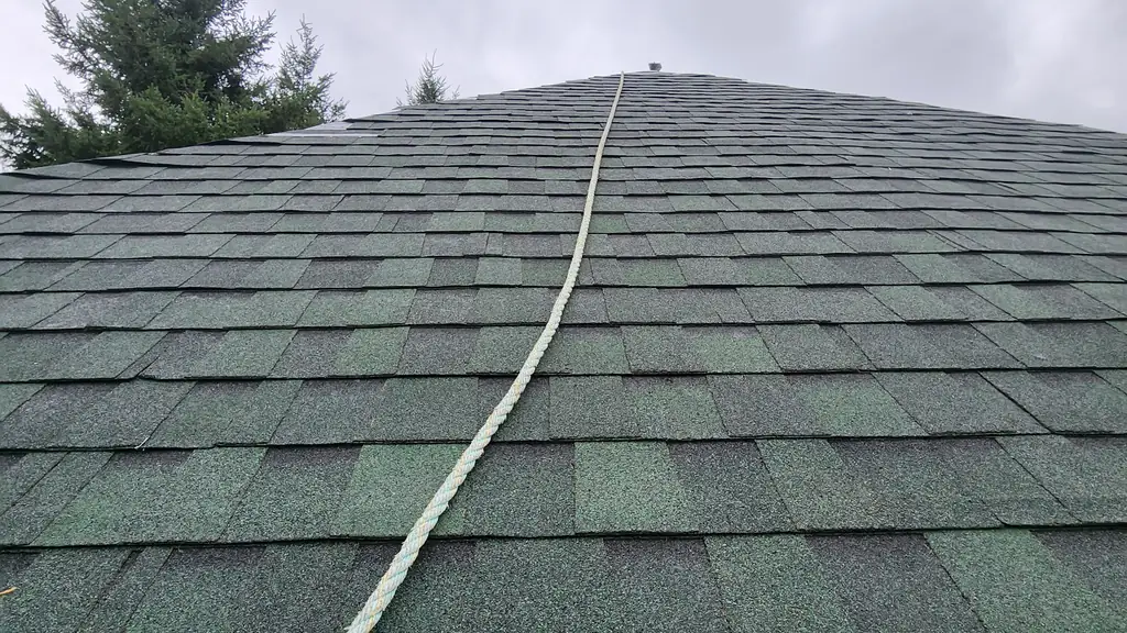 Looking straight up along the ridge of a dark green architectural shingle roof, with a yellow safety rope running up to a small vent cap at the peak. Fraser Roofing