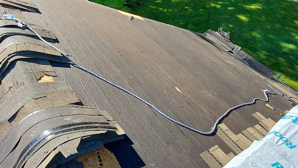 An on-roof shot along the eave of an aged brown shingle roof mid tear-off. Fraser Roofing