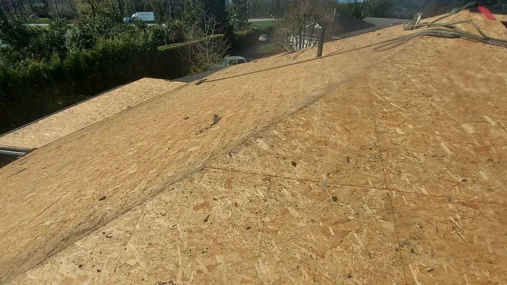 View along a large plywood-decked roof under a partly cloudy blue sky. Fraser Roofing