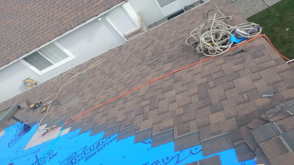 A roof mid-tear-off shows old brown asphalt shingles next to a section of blue synthetic underlayment printed with RoofinAid StormTread branding. Fraser Roofing