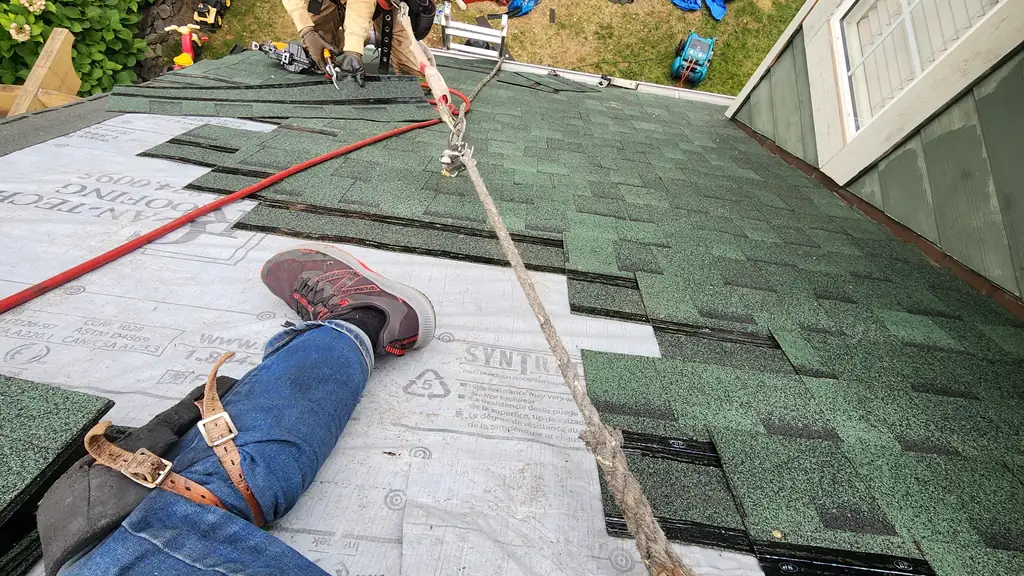 A roofer in a tan jacket and red cap, wearing a full safety harness. Fraser Roofing