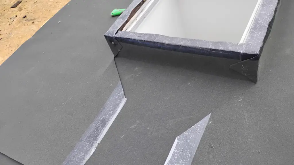 Close-up of a skylight curb being flashed with black peel-and-stick membrane on a flat grey roof surface. Fraser Roofing