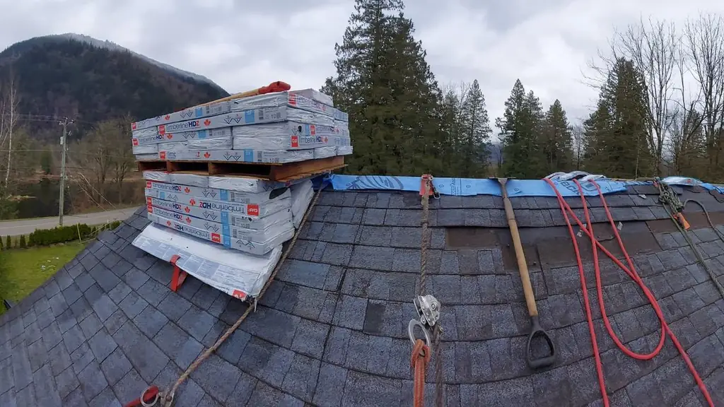 A wide, slightly stitched/panoramic view across a shingle roof with bundles of 'Timberline HDZ' shingles stacked near the ridge. Fraser Roofing