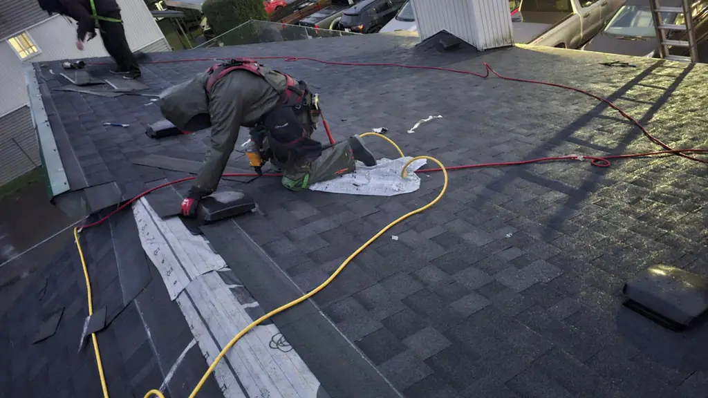 Two workers on a low-slope asphalt shingle roof of a commercial building at dusk. Fraser Roofing