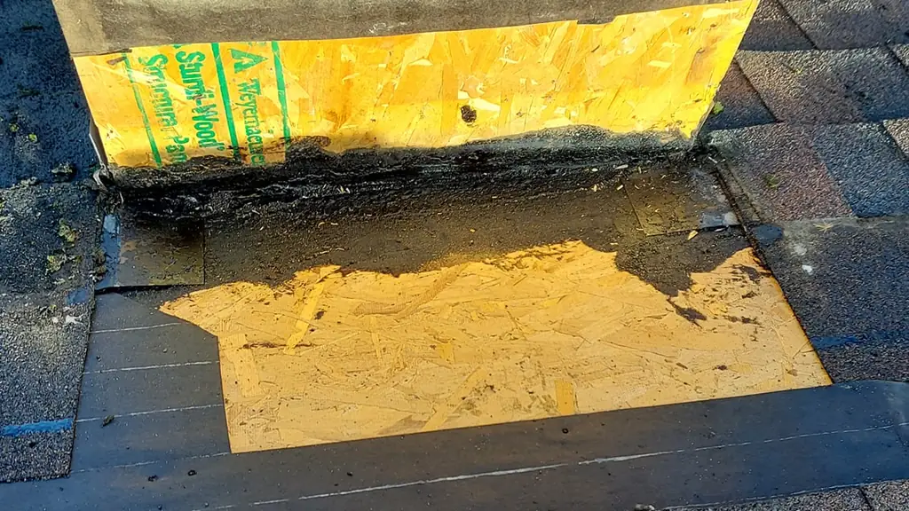Close detail of ice-and-water shield membrane and dark sealant applied around the base of a chimney chase. Fraser Roofing
