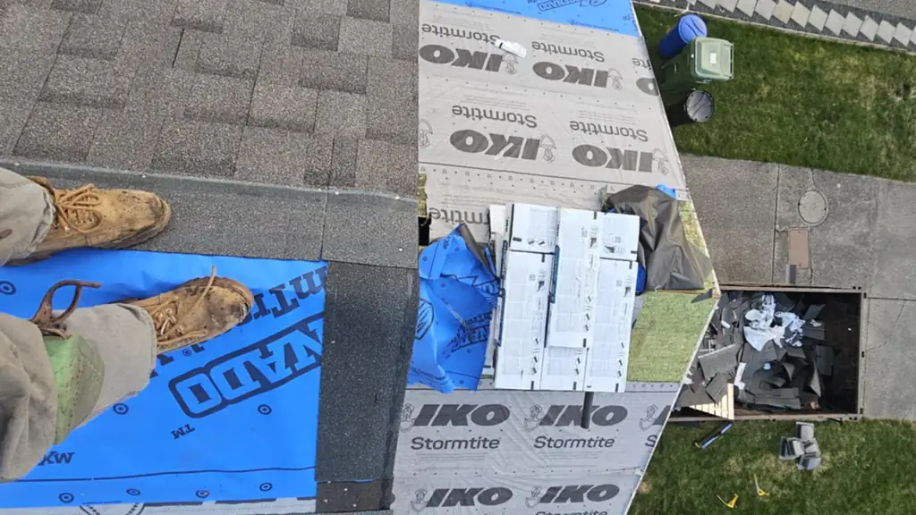 A worker's boots stand on blue RoofinAid StormTread synthetic underlayment at a roof edge. Fraser Roofing
