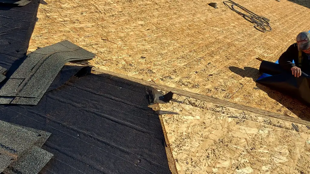 Steep roof slope mid tear-off: bare OSB decking exposed on the upper section with a stack of pulled shingles at the ridge. Fraser Roofing