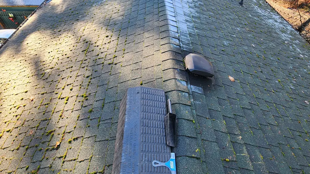 A view down a moss-speckled roof ridge with several vents including two turbine vents and plumbing stacks. Fraser Roofing