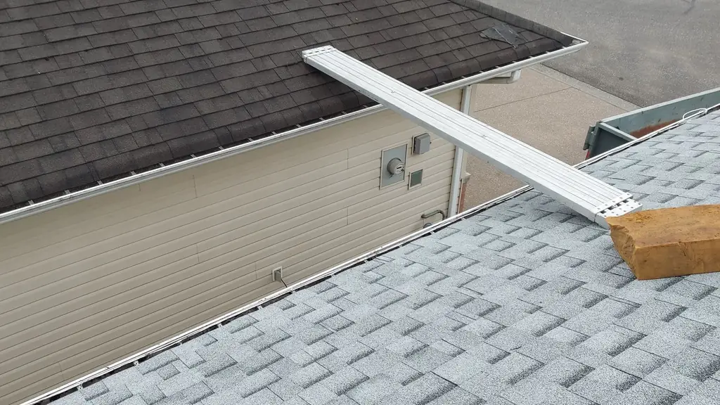 An on-roof shot showing a bundle of IKO Cambridge shingles staged on the ridge of a brown roof. Fraser Roofing