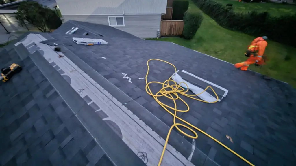 A dusk view along an asphalt shingle roof shows a coiled yellow hose, a yellow power tool, and an IKO Hip & Ridge shingle box in the foreground. Fraser Roofing