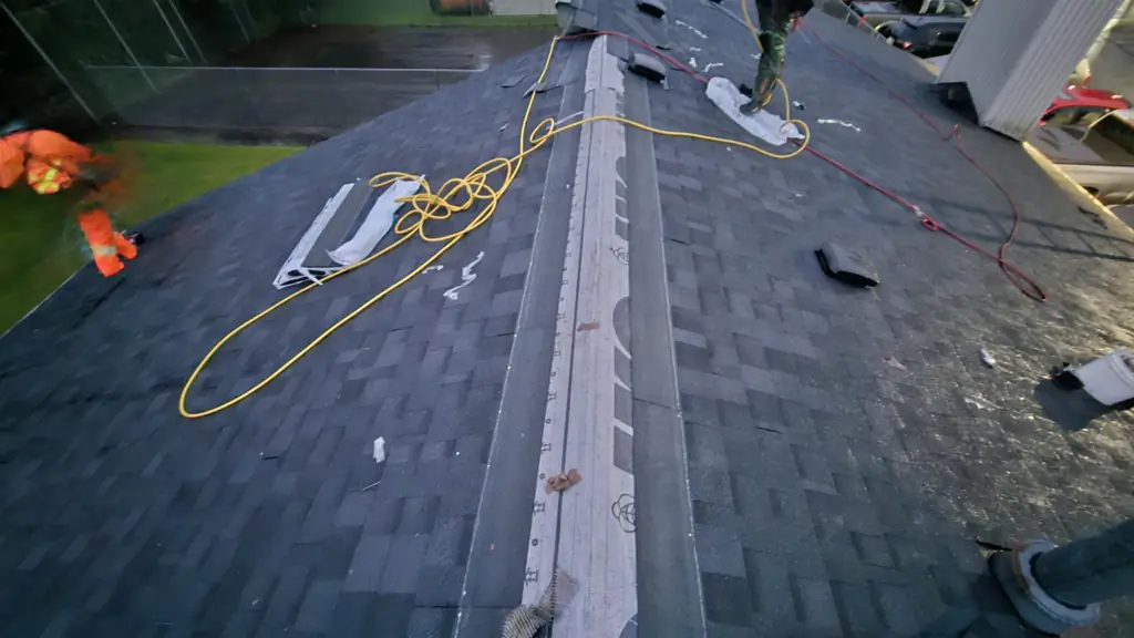 An on-roof shot mid tear-off with one worker in camo-patterned coveralls and another worker in blurred motion wearing orange safety gear. Fraser Roofing
