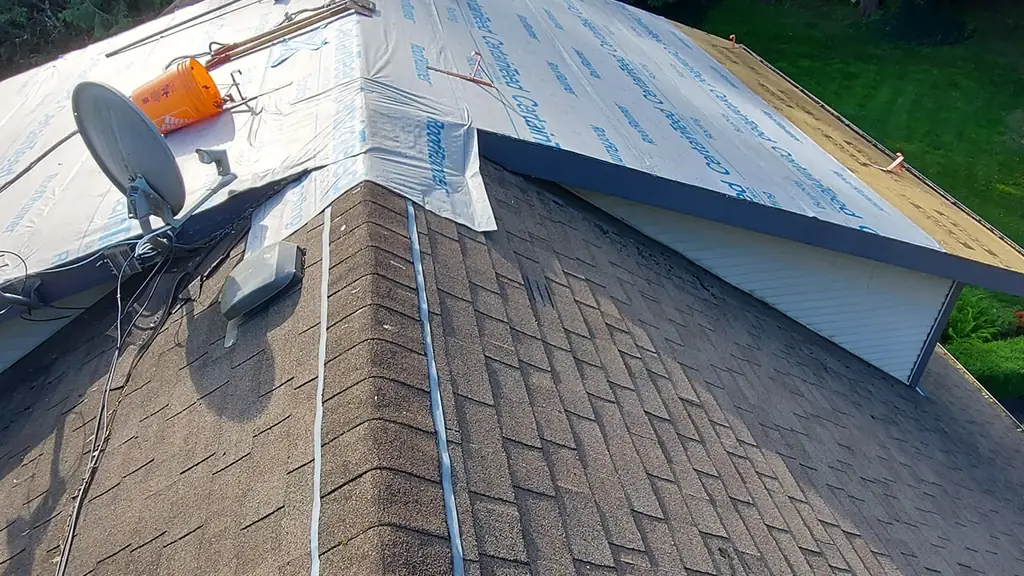 A shot looking down a hip roof ridge covered in worn brown asphalt shingles, with a yellow roof-anchor safety strap in the foreground. Fraser Roofing