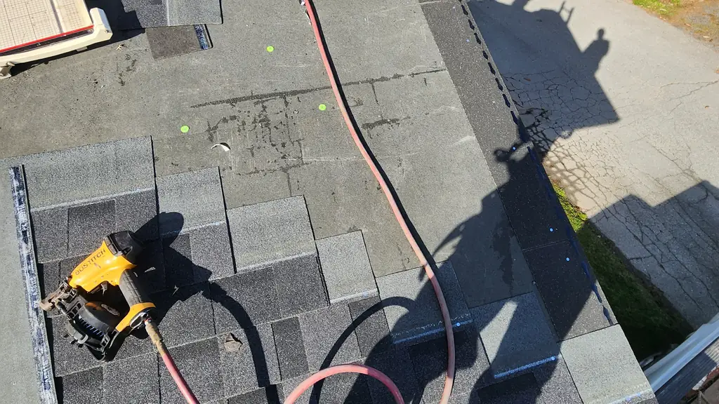 An on-roof shot of a yellow Bostitch pneumatic roofing nailer with a pink air hose lying on top of freshly installed grey shingles. Fraser Roofing