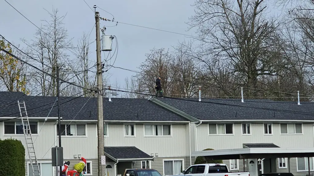 A worker walks along the ridge of a newly shingled dark charcoal roof on a row of townhouses, seen from the street below. Fraser Roofing