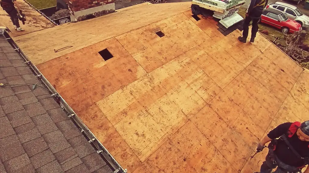 A genuine decking tear-off and replacement in progress: bare OSB plywood covers most of the roof around a large brick chimney. Fraser Roofing