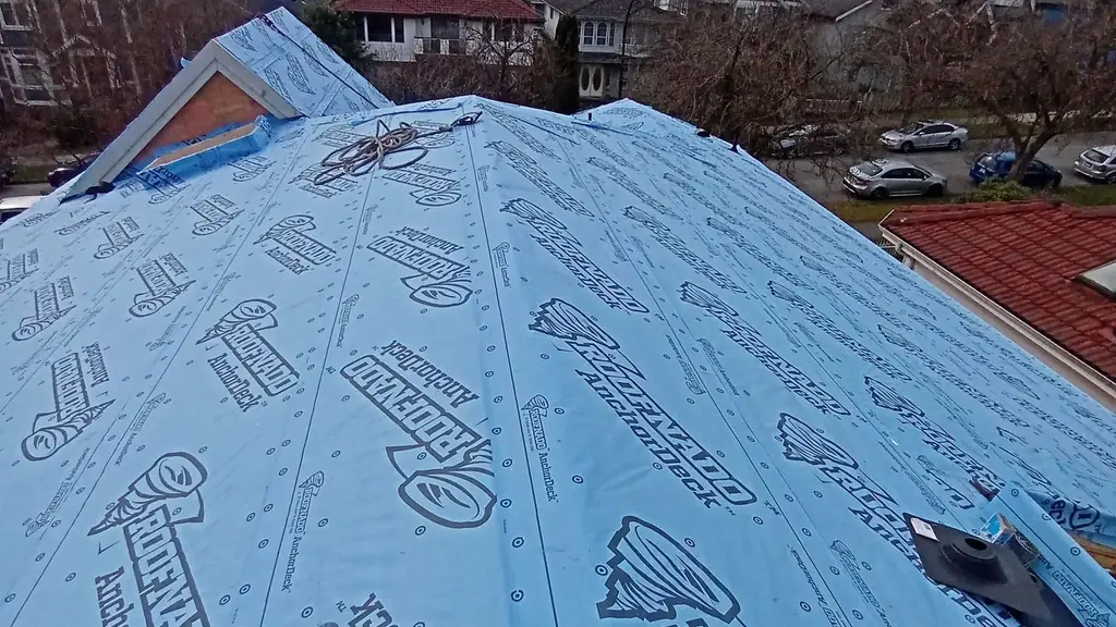 Close-up looking down a steep roof slope fully wrapped in blue 'Roofnado AnchorDeck' branded synthetic underlayment. Fraser Roofing