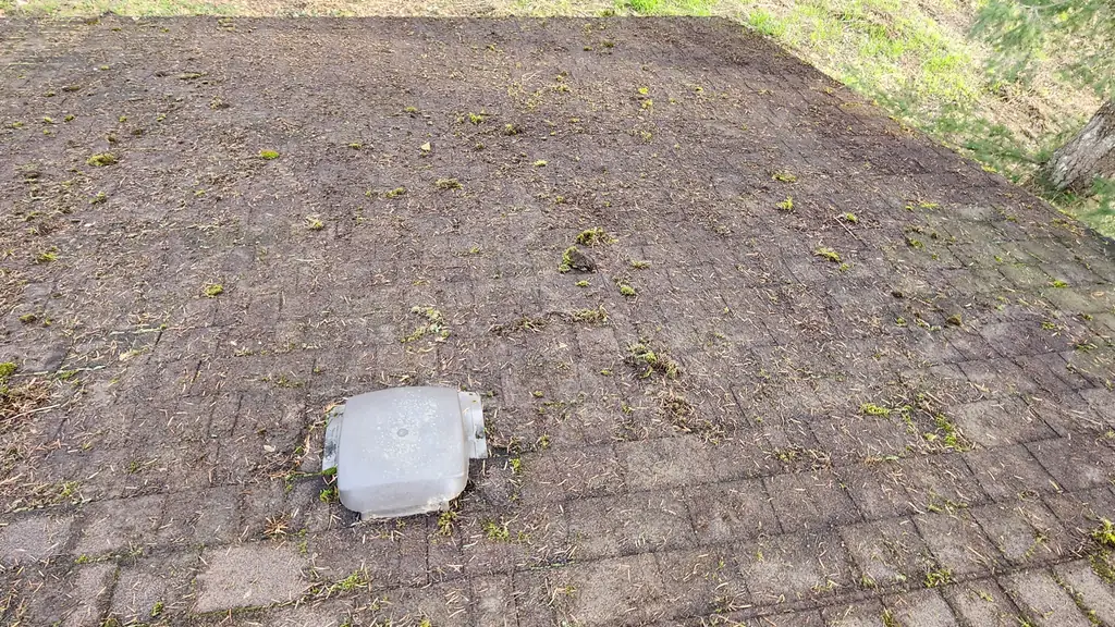 A dirt-covered, low-slope asphalt shingle roof section is shown with sparse moss growth and a plastic roof vent cap in the middle. Fraser Roofing