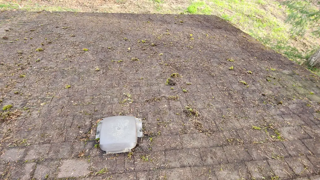 Overhead view standing on a dirty asphalt shingle roof with a white dome vent cap in view, a wooded hillside beyond the roof edge. Fraser Roofing