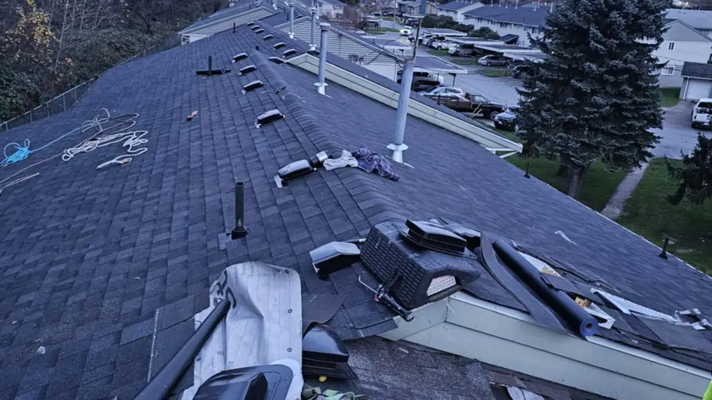 A dusk shot along a roof ridge mid re-roof, with a row of old plastic pipe boots and vents piled up after being removed. Fraser Roofing