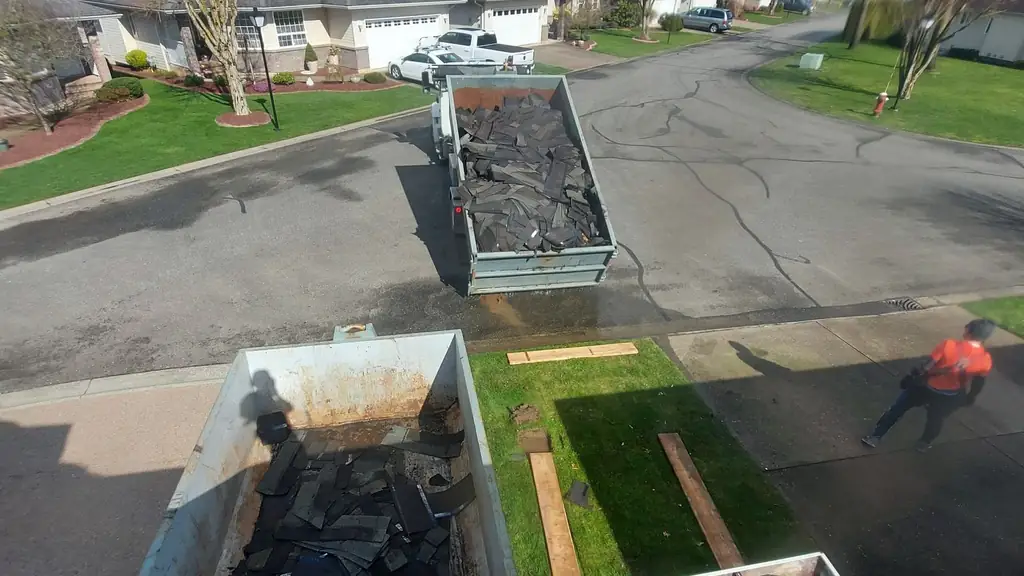 Aerial view down onto two open-top dump trailers parked on the street, both piled with torn-off dark shingle debris. Fraser Roofing