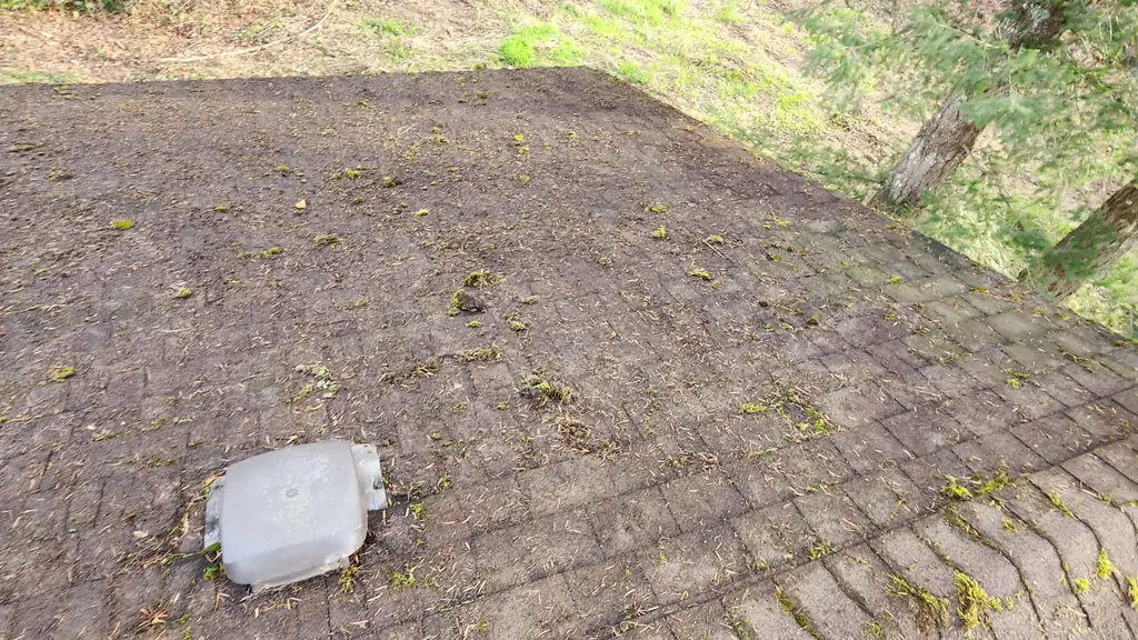 Overhead view of a dirty, debris-covered asphalt shingle roof surface with a white dome-shaped plumbing vent cap in the middle distance. Fraser Roofing