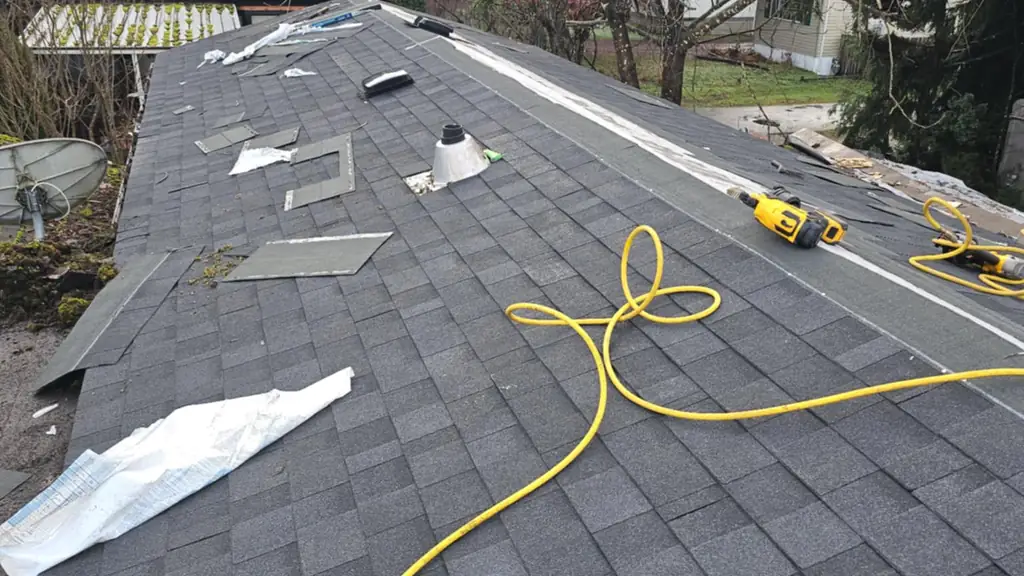 A long straight section of roof, nearly finished in dark grey shingles, photographed on a wet, overcast day. Fraser Roofing