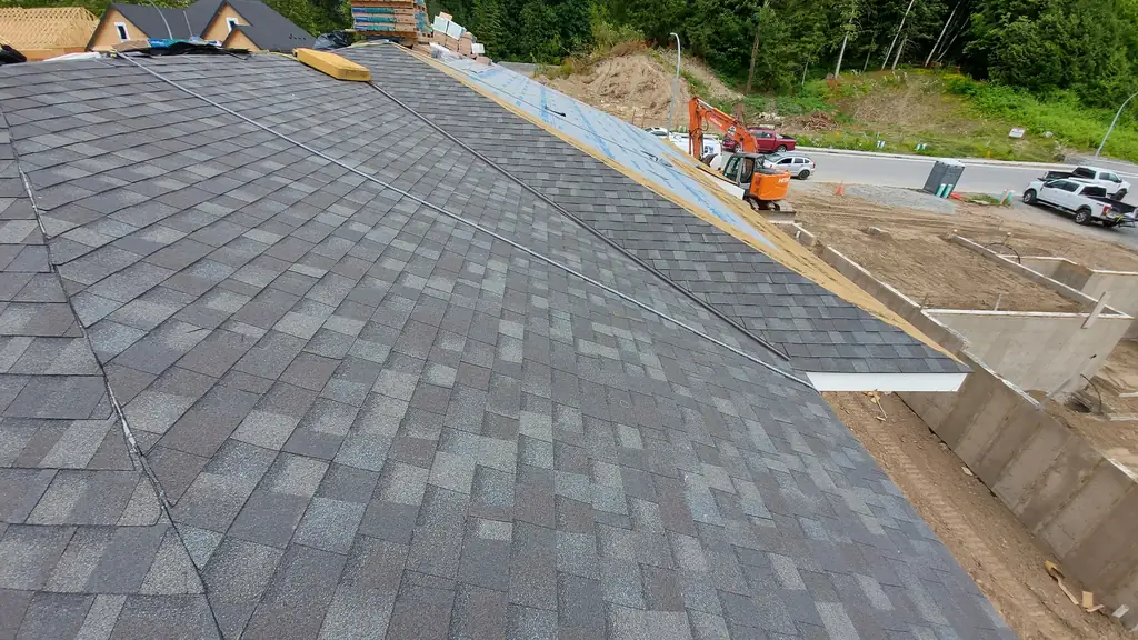 Wide view standing on a new gray dimensional shingle roof, with bundles of shingles stacked at the ridge and a neighbouring house still under. Fraser Roofing