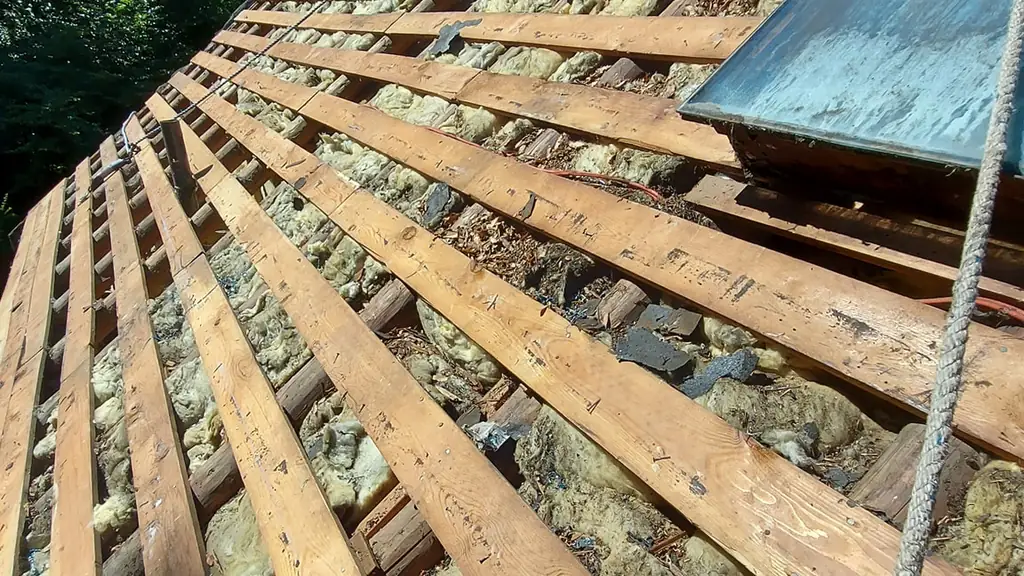 Looking straight up along exposed roof rafters on what appears to be a cottage-style roof mid tear-off to bare structure. Fraser Roofing