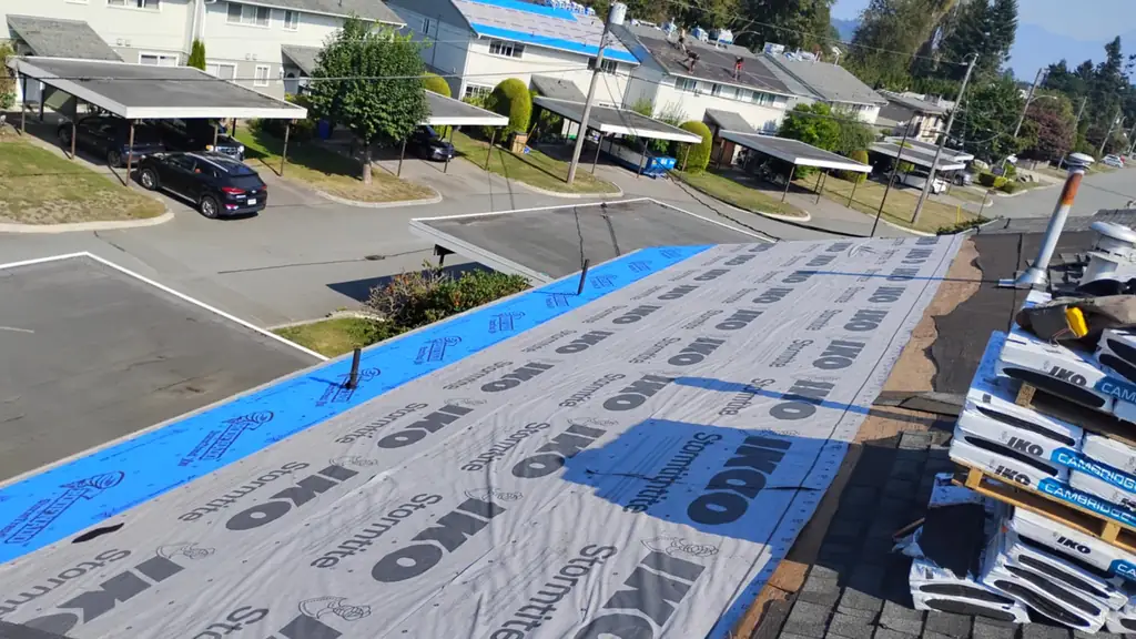 High vantage looking down a long underlayment-covered roof run with a blue IKO synthetic strip along the near edge. Fraser Roofing