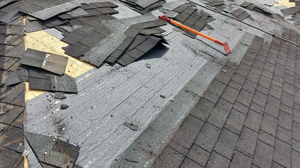 A view along a roof slope during tear-off, with torn black shingles piled and scattered across exposed underlayment/decking on the upper portion. Fraser Roofing