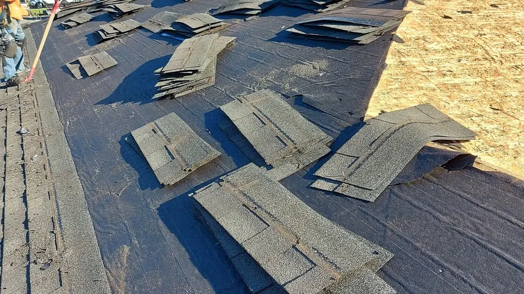 A residential roof mid-tear-off shows bare OSB decking exposed on one slope, with old asphalt shingles still scattered across felt paper on the rest. Fraser Roofing
